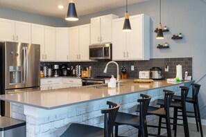 A modern kitchen with white cabinets, stainless steel appliances, a large island with bar stools, and pendant lighting. - Lakefront 9 Bedroom Villa: Arcade, Themed Rooms, Lazy River (Kissimmee)