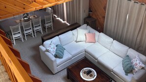 Un saló d'estil loft amb sostre de fusta, un sofà seccional blanc, una taula de centre i una zona menjador amb cadires i taula.