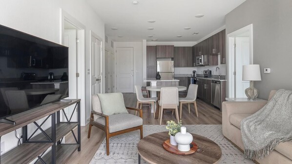 A modern living room with a TV, seating, a dining area, and a kitchen.