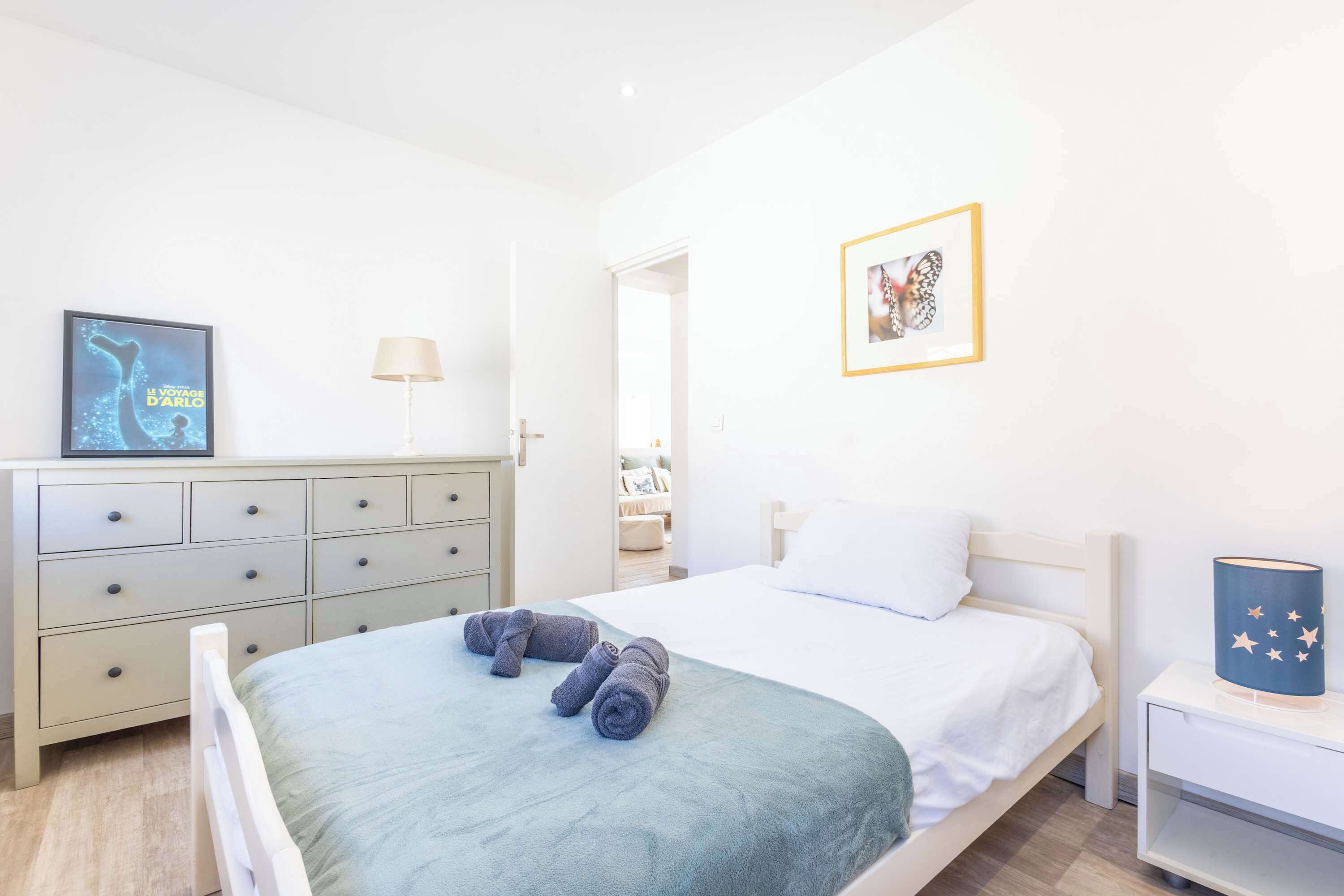 Habitación de hotel con cama, cómoda, mesita de noche, lámpara y un cuadro en la pared.