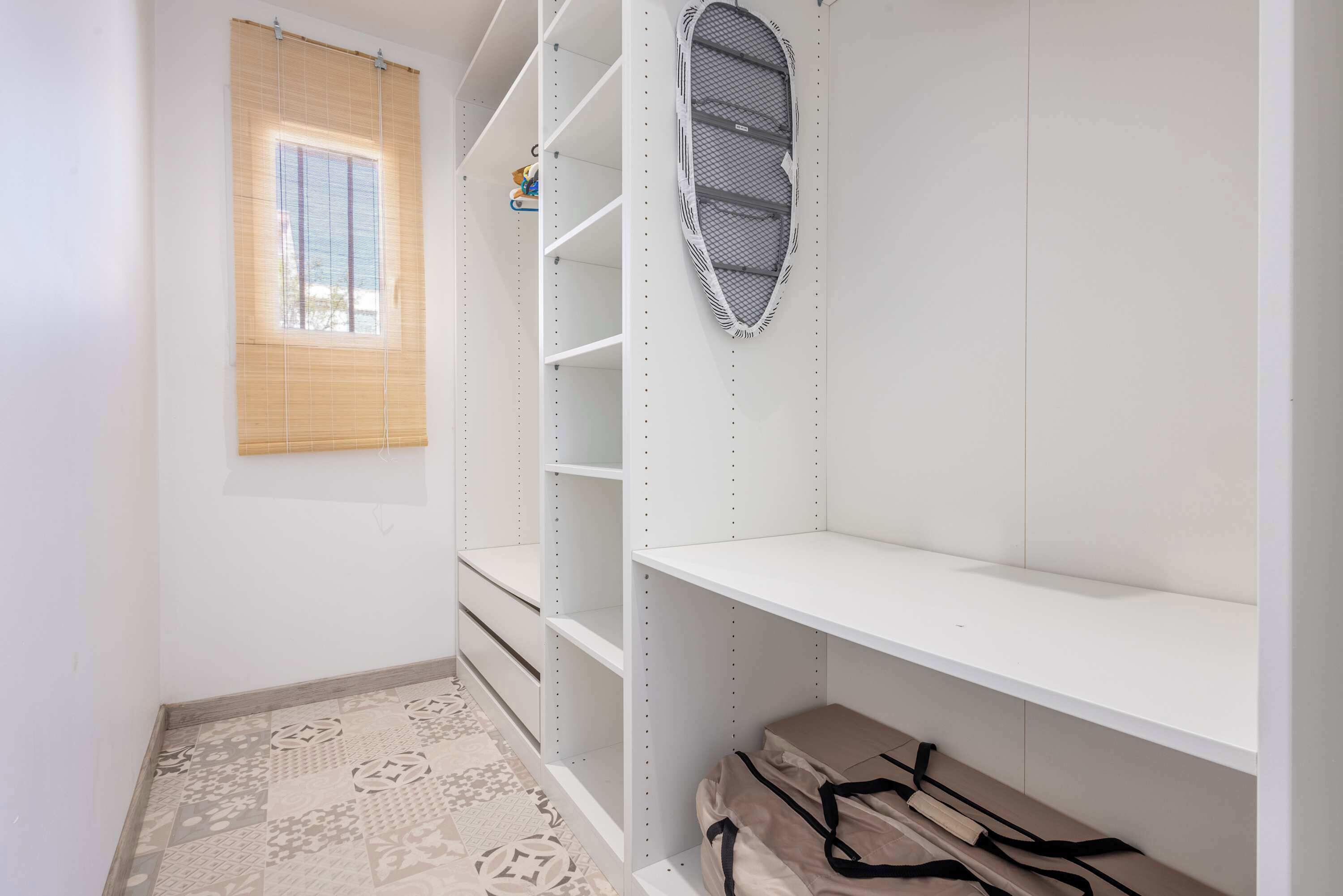 A room with a window, a white shelf unit, a patterned floor, and a bag on the floor.
