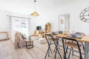 A modern living room with a sofa, a coffee table, a TV, and a dining area with a wooden table and chairs. - Valras-Plage Renovated House w/ Terrace, Close (Valras-Plage)
