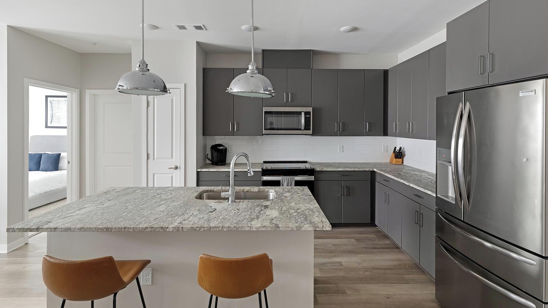 A modern kitchen with grey cabinets, stainless steel appliances, a marble countertop, and pendant lighting.