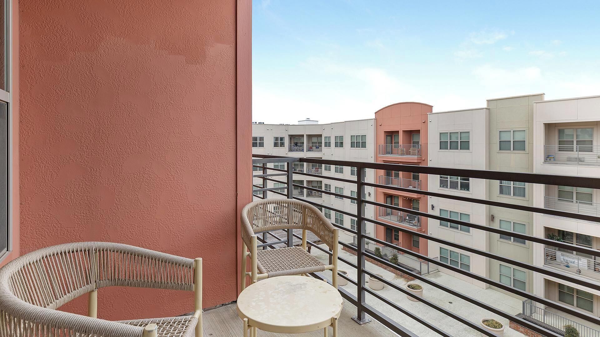 A balcony with two wicker chairs and a small table, overlooking a multi-story building with balconies.
