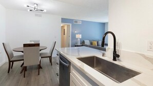 A modern kitchen with a sink, countertop, and dining area with chairs and a table. - Landing | Chic 2BD, Courtyard (Paradise)