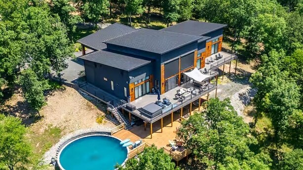 Una casa moderna de dos pisos con piscina, rodeada de árboles frondosos.