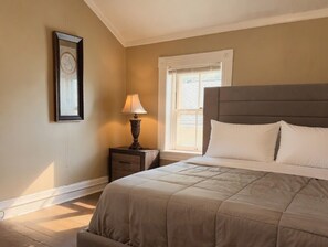 A bedroom with a bed, nightstand, lamp, and a framed picture on the wall.