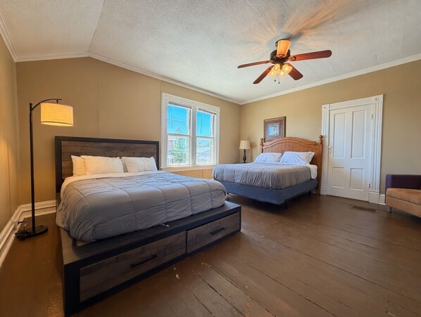 A bedroom with two beds, a ceiling fan, a floor lamp, and a door.