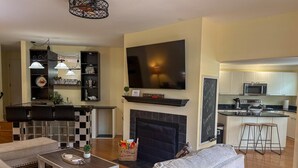 Uma sala de estar com lareira, uma cozinha equipada com micro-ondas e um espaço bar.
