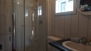 A bathroom with a glass-enclosed shower, a toilet, a sink with a towel, and a window. - Escape in the heart of Miller Zoo | Sheira Shack (Frampton)