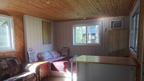 A room with a wooden ceiling, a bed with patterned bedding, a wooden bench, a small table, and a window with a view of trees. - Escape in the heart of Miller Zoo | Sheira Shack (Frampton)