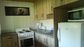 A kitchen with wooden cabinets, a stove, a microwave, and a coffee maker. - Escape in the heart of Miller Zoo | Sheira Shack (Frampton)
