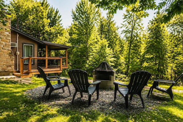 A cabin with a deck, a fire pit, and three Adirondack chairs.