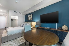 Une chambre d’hôtel moderne avec un lit, une table à manger ronde, un téléviseur et un mur d’accent bleu.