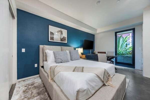 Une chambre moderne équipée d’un lit, d’un bureau, d’une télévision et d’une grande fenêtre donnant sur un paysage verdoyant.