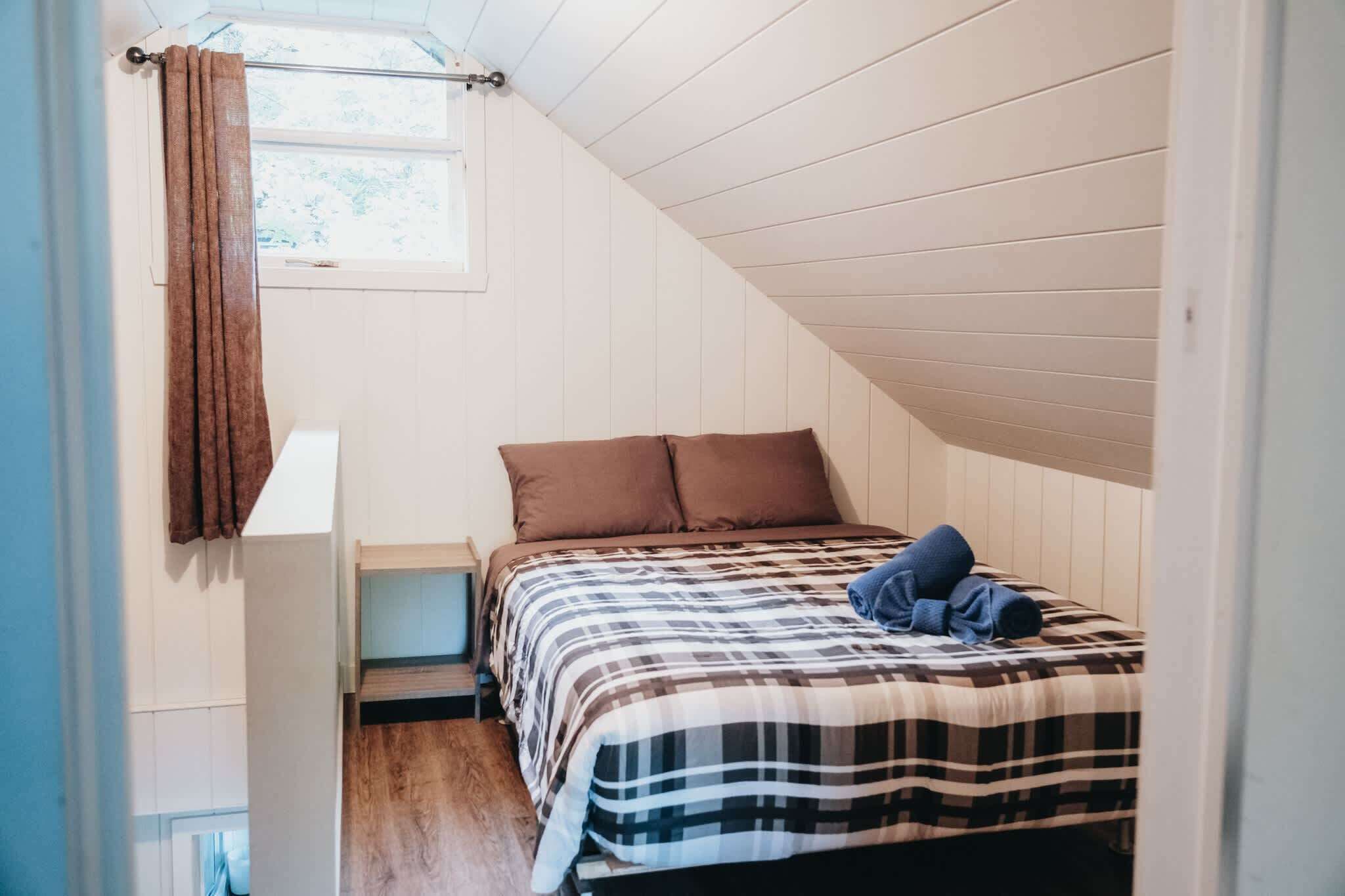 Une chambre à coucher avec un lit, des rideaux marron, une fenêtre et un plafond en pente.