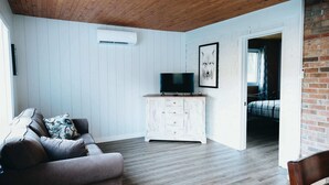 A living room with a sofa, TV, white cabinet, and a framed picture on the wall. - River & Miller Zoo | Louna-Nuage Shack (Frampton)