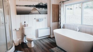 A bathroom with a bathtub, toilet, shower, and a large window. - River & Miller Zoo | Louna-Nuage Shack (Frampton)