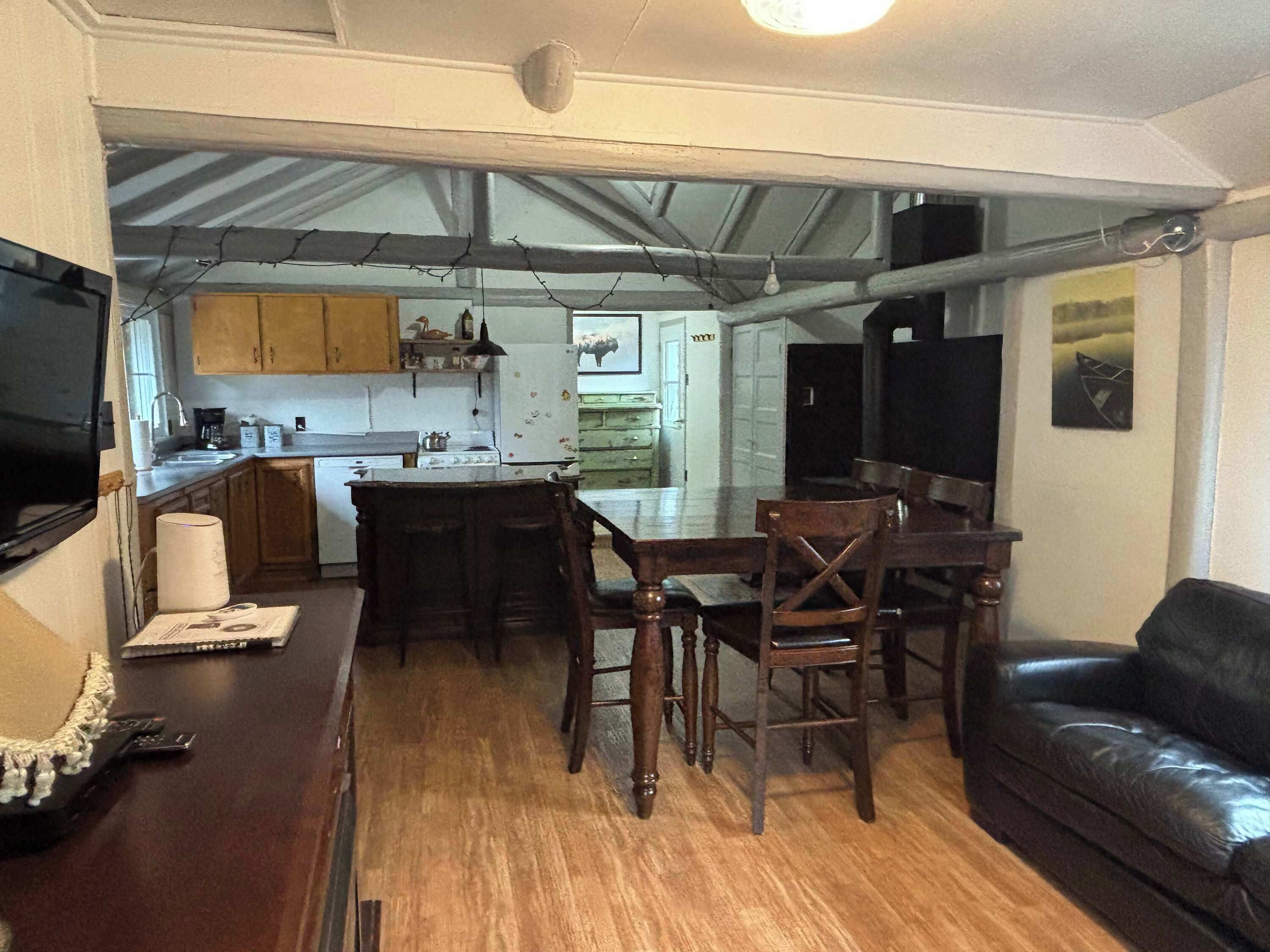 A compact kitchen with a dining area, a black leather couch, and a TV mounted on the wall.