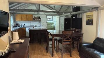 A compact kitchen with a dining area, a black leather couch, and a TV mounted on the wall.