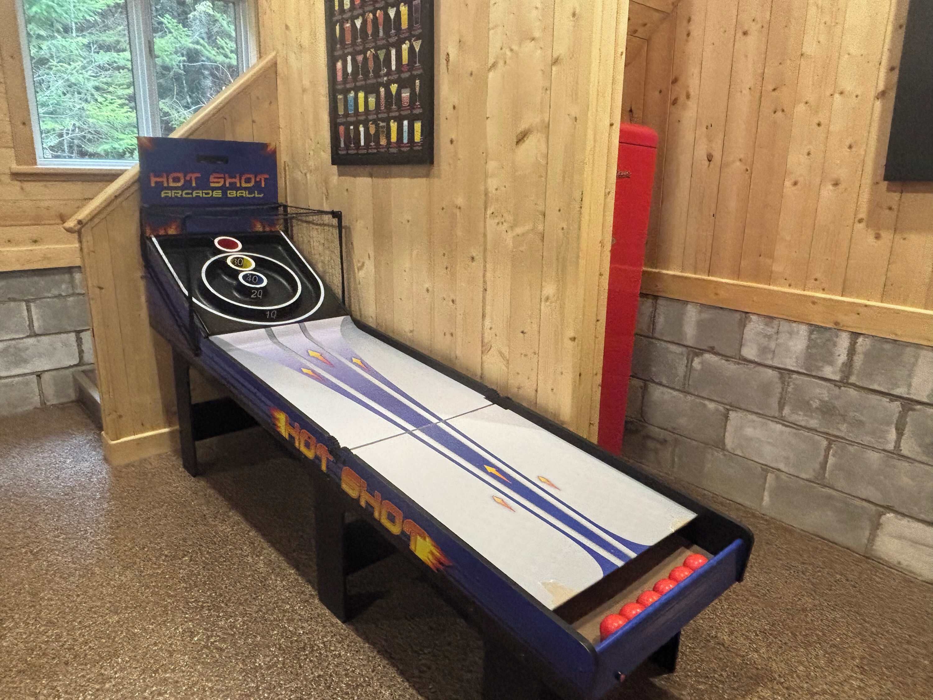 Une table de jeu d’arcade « Hot Shot », avec un sol en bois et une fenêtre en arrière-plan.