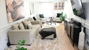 Un salon comprenant un canapé, un pouf, une table basse et un téléviseur.