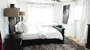 Une chambre à coucher avec un lit, un ventilateur de plafond, une table de chevet, une lampe et un tableau au mur.