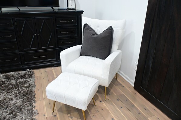A white armchair with a matching ottoman, a dark wooden cabinet, and a fluffy gray rug. - Platinum Stay ATL …20 mins to Mercedes Benz Stadium. (Fairburn)