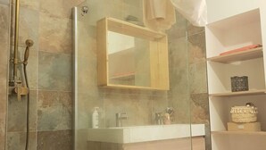 Un baño moderno con cabina de ducha de vidrio, tocador con espejo y estante con artículos de aseo.