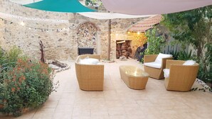 Un patio con mobiliario de mimbre, una pared de piedra y suelo de baldosas.