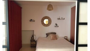 Un dormitorio con una cama, un espejo redondo, una mesita de noche, una lámpara y una lámpara colgante.