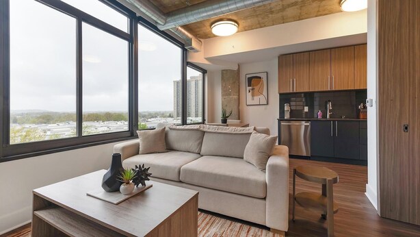 En moderne stue med sofa, sofabord og udsigt over bybilledet gennem store vinduer.
