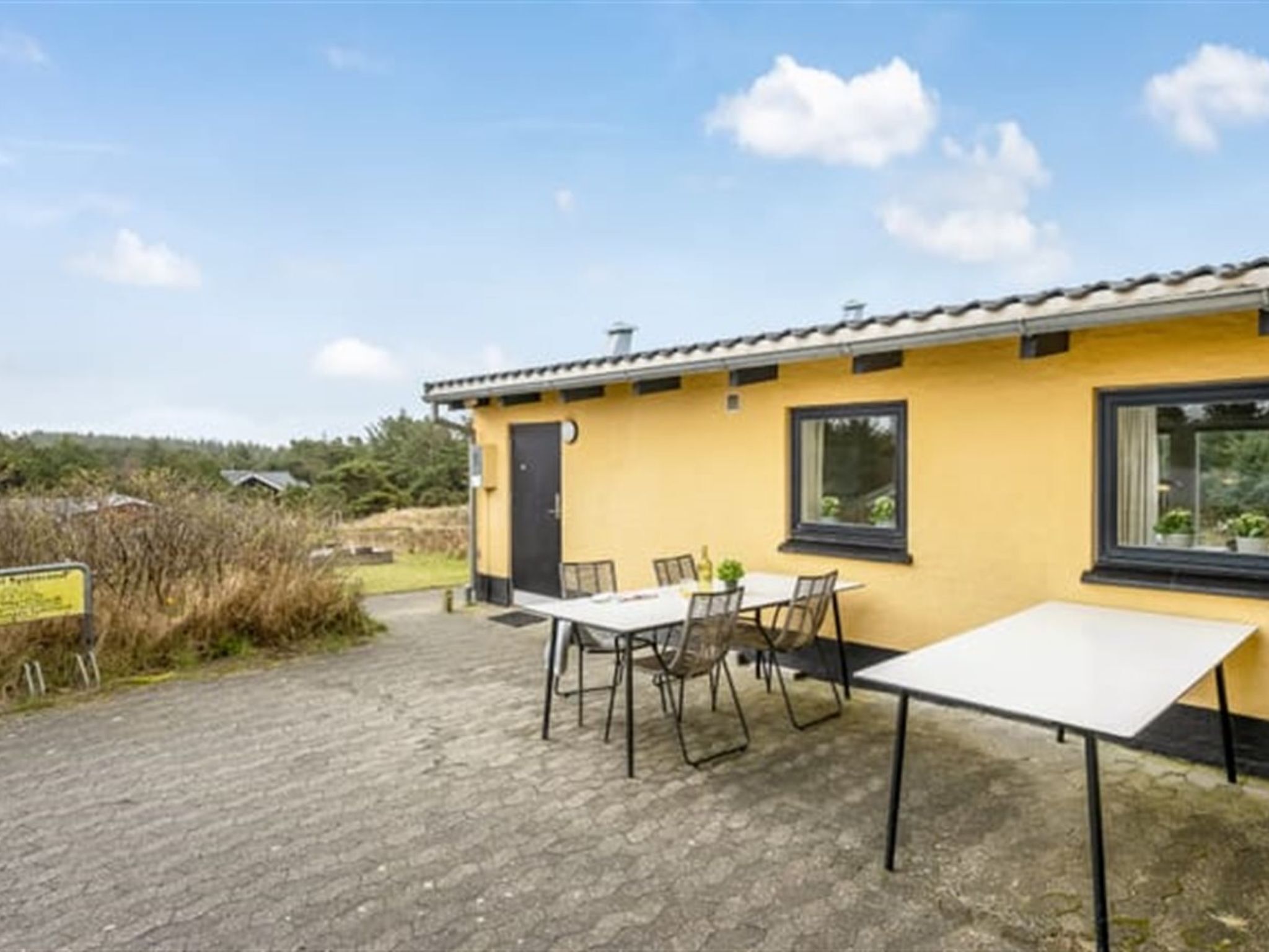 Un edificio amarillo con un patio empedrado, una mesa con sillas y una ventana.