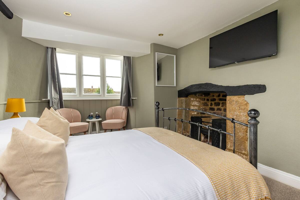 Une chambre d’hôtel avec un lit, une télévision, une cheminée, une fenêtre et une chaise.