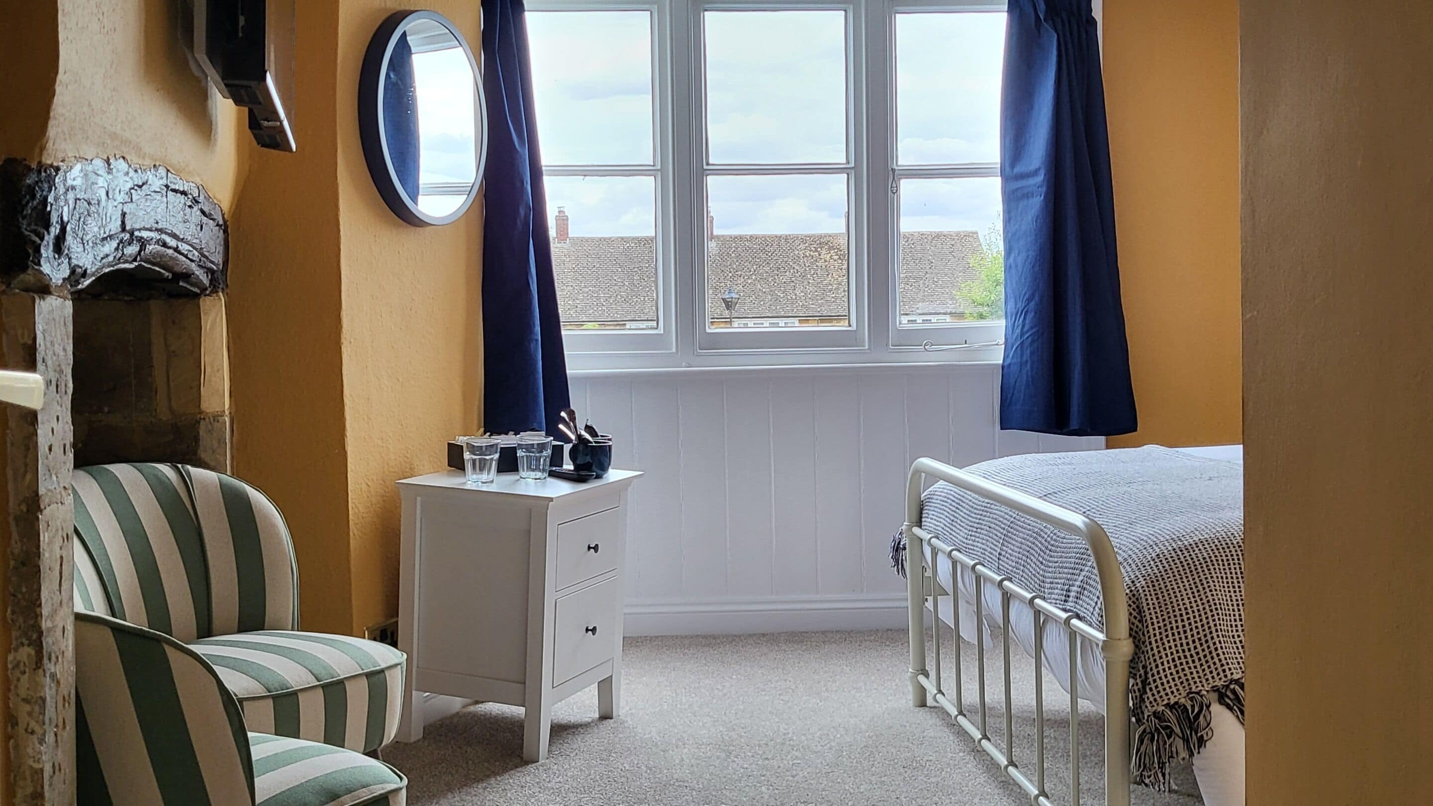 A bedroom with a bed, a chair, a dresser, a mirror, and a window with curtains.