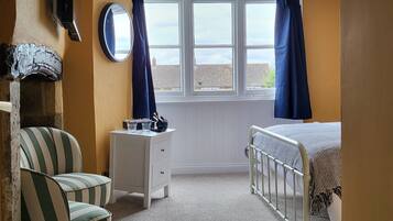 A bedroom with a bed, a chair, a dresser, a mirror, and a window with curtains.