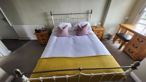 A bedroom with a bed, bedside tables, a wooden dresser, and a radiator. - Unicorn Inn (Deddington)