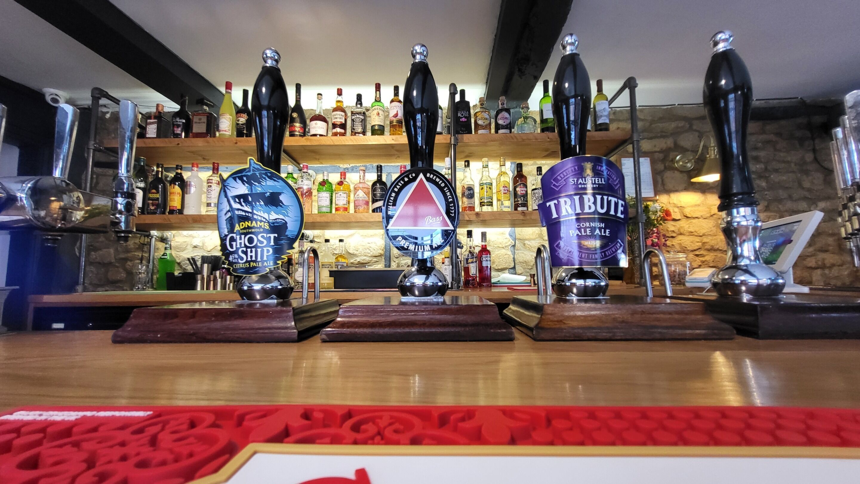 A bar with three tap handles, each with a distinct label. Behind the bar, shelves are stocked with various bottles.