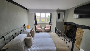 A bedroom with a bed, two chairs, a small table, a fireplace, and a window with curtains. - Unicorn Inn (Deddington)