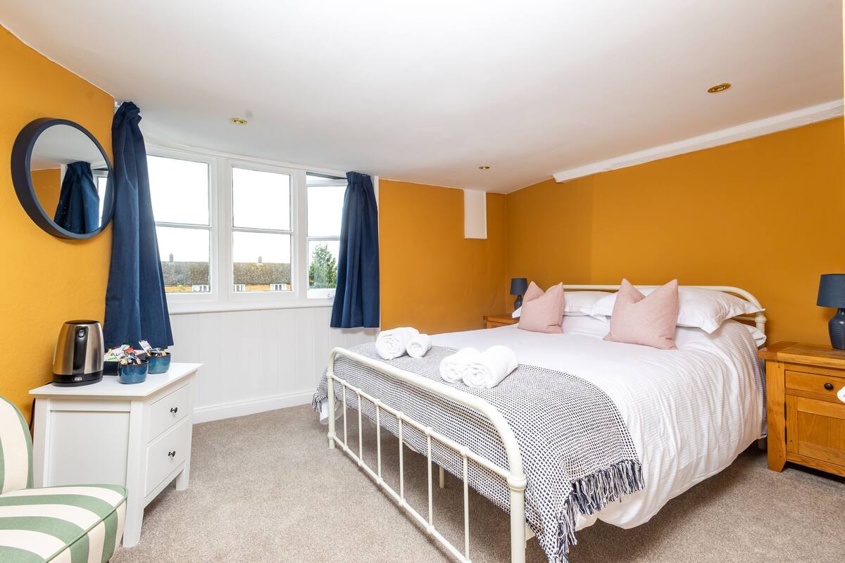 Une chambre à coucher avec un lit, des tables de chevet, un miroir et une fenêtre avec des rideaux.