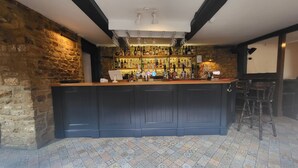 A bar area with a wooden counter, stone walls, and a tiled floor. - Unicorn Inn (Deddington)