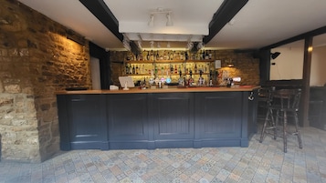 A bar area with a wooden counter, stone walls, and a tiled floor.