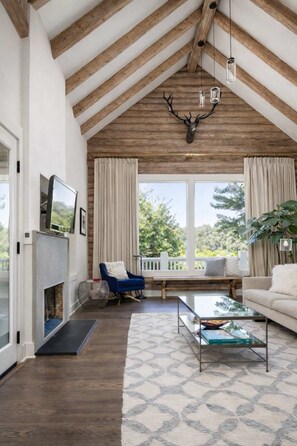 A spacious living room with a high ceiling, wooden beams, a fireplace, a sofa, a coffee table, and a television. - The Anderson - Calistoga , Pool, Near Vineyards (Calistoga)