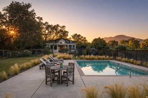 A backyard with a swimming pool, a dining table with chairs, and a house in the background. - The Anderson - Calistoga , Pool, Near Vineyards (Calistoga)