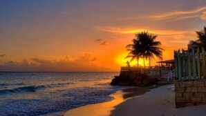 Eine Strandansicht mit Sonnenuntergang, Palmen und einem Holzzaun.