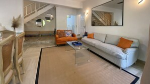 Ein Wohnzimmer mit Sofa, Couchtisch und Sesseln. Eine Treppe führt zu einer weiteren Ebene.