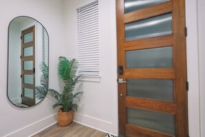 A hallway with a wooden door, a mirror, and a potted plant. - Solara/3BRs/FIFA/Sleeps14/NRG/HTX/Arcade/LaserTag (Houston)