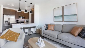 Ein modernes Wohnzimmer mit grauem Sofa, einem Couchtisch und einer Küchenzeile im Hintergrund.