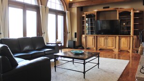 A living room with a black leather sofa, a coffee table with a blue bowl, wooden cabinets, and a television. - High-End Waterfront Estate in Stratford | Relax, Unwind, Enjoy Views (Stratford)