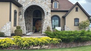 A house with a stone archway entrance, a stone facade, and a well-maintained front yard with yellow flowering plants. - High-End Waterfront Estate in Stratford | Relax, Unwind, Enjoy Views (Stratford)